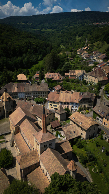Aerial view of Romainm&ocirc;tier Abbey s terracotta rooftops nestled in a valley embraced by dark green forests Romainm&ocirc;tier Envy Vaud Switzerland.