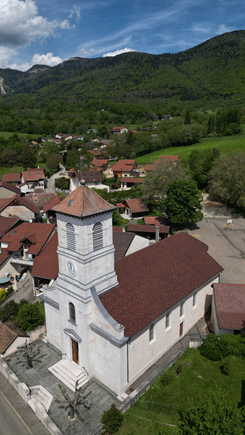 Aerial view of the historic stone church with its clock tower and red tiled roof in the village of Vesancy Auvergne Rhone Alpes France. Aerial view of the historic stone church with its clock tower and red tiled roof in the village of Vesancy Auvergne Rhone Alpes France.