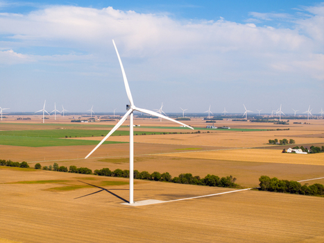 Aerial view of wind turbines in a vast agricultural landscape with golden fields and green patches under a blue sky in Wolcott Indiana United States.