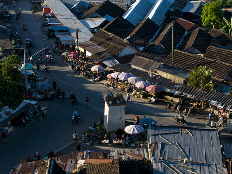 Aerial view of a bustling street market with vendors under colorful umbrellas motorbikes and traditional dark tiled rooftops Kemalang Central Java Indonesia.