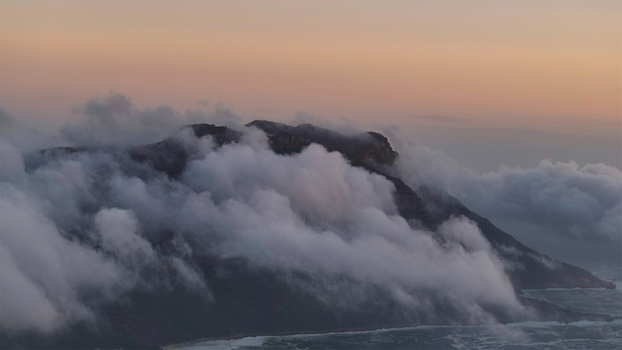 Aerial view of Table Mountain shrouded in thick white clouds rolling over the peaks during a soft sunset in Cape Town Western Cape South Africa. Aerial view of Table Mountain shrouded in thick white clouds rolling over the peaks during a soft sunset in Cape Town Western Cape South Africa.