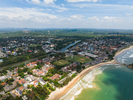 Aerial view of the Nilwala River flowing through the urban landscape and lush greenery towards the sandy beach and turquoise ocean in Matara Southern Province Sri Lanka. Aerial view of the Nilwala River flowing through the urban landscape and lush greenery towards the sandy beach and turquoise ocean in Matara Southern Province Sri Lanka.
