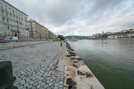 View of the Shoes on the Danube Bank memorial with bronze shoes placed along the riverbank cobblestone promenade and the Danube river in Budapest Hungary.