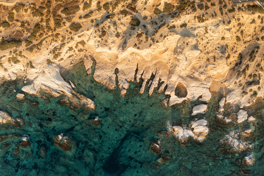 Aerial view of rugged cliffs meet the turquoise sea the sun casting long shadows on the white rocks creating a dramatic coastal scene Fira Thira Greece. Aerial view of rugged cliffs meet the turquoise sea the sun casting long shadows on the white rocks creating a dramatic coastal scene Fira Thira Greece.
