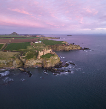 Aerial view of Tantallon Castle on a rocky cliff overlooking the sea under a pink sunset sky North Berwick Scotland United Kingdom.