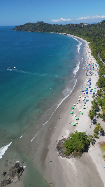 Aerial view of the beach with colorful umbrellas contrasting against the deep blue sea and lush green coastline Quepos Puntarenas Province Costa Rica. Aerial view of the beach with colorful umbrellas contrasting against the deep blue sea and lush green coastline Quepos Puntarenas Province Costa Rica.