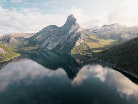 Aerial view of the iconic Stetind mountain reflecting in the calm waters of the fjord surrounded by rugged slopes and lush green hills in Kjopsvik Nordland Norway. Aerial view of the iconic Stetind mountain reflecting in the calm waters of the fjord surrounded by rugged slopes and lush green hills in Kjopsvik Nordland Norway.
