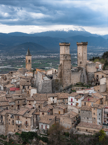 Aerial view of the historic Caldora Castle towers and terracotta rooftops of the medieval village set against snow capped mountains in Pacentro Abruzzo Italy. Aerial view of the historic Caldora Castle towers and terracotta rooftops of the medieval village set against snow capped mountains in Pacentro Abruzzo Italy.