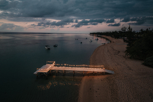 Aerial view of a wooden pier decorated with glowing string lights on a sandy beach at dusk with small boats anchored in the calm bay in Mauritius. Aerial view of a wooden pier decorated with glowing string lights on a sandy beach at dusk with small boats anchored in the calm bay in Mauritius.