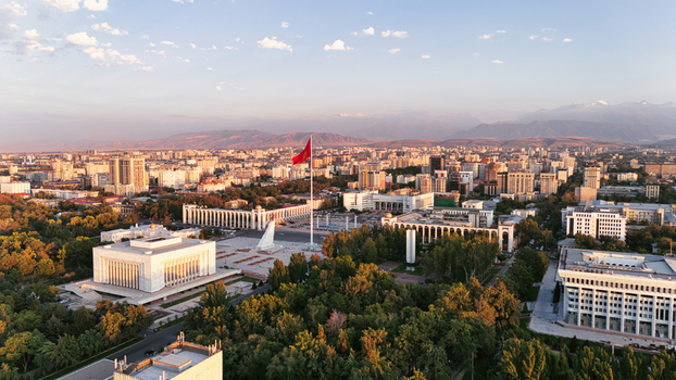 Aerial view of Ala Too Square with the national flag historic government buildings lush trees and urban architecture under sunset light in Bishkek City Kyrgyzstan.
