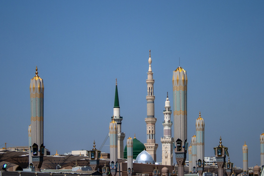 View of the minarets and the iconic green dome of Al Masjid e Nabawi under a clear blue sky in Madinah Al Madinah Province Saudi Arabia.