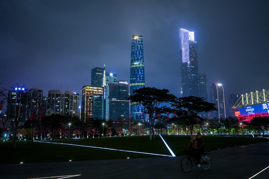 Guangzhou Guangdong Province China 24 February 2024 View of the illuminated skyline at night with modern skyscrapers and a person riding a bicycle through a park in the foreground. Guangzhou Guangdong Province China 24 February 2024 View of the illuminated skyline at night with modern skyscrapers and a person riding a bicycle through a park in the foreground.