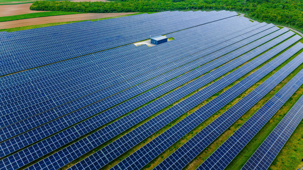 Aerial view of a large solar farm with rows of blue photovoltaic panels and a central utility building surrounded by green fields and lush forests Sabac Vojvodina Serbia.