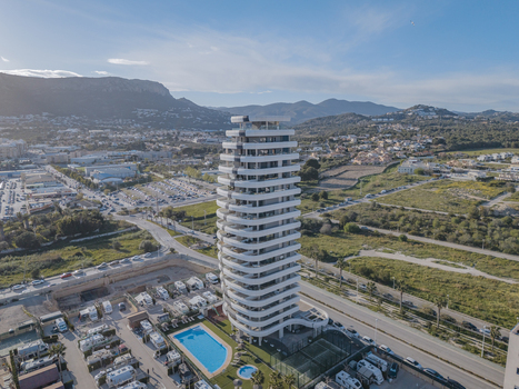 Aerial view of a modern high rise residential building with curved balconies a swimming pool and surrounding urban landscape in Calp Valencian Community Spain. Aerial view of a modern high rise residential building with curved balconies a swimming pool and surrounding urban landscape in Calp Valencian Community Spain.