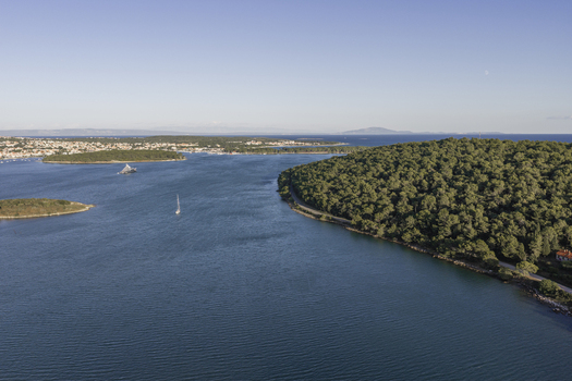 Aerial view of the coastline of Premantura featuring the lush pine forests of Cape Kamenjak calm blue waters of the Adriatic Sea and small sailboats in Premantura Istria County Croatia. Aerial view of the coastline of Premantura featuring the lush pine forests of Cape Kamenjak calm blue waters of the Adriatic Sea and small sailboats in Premantura Istria County Croatia.