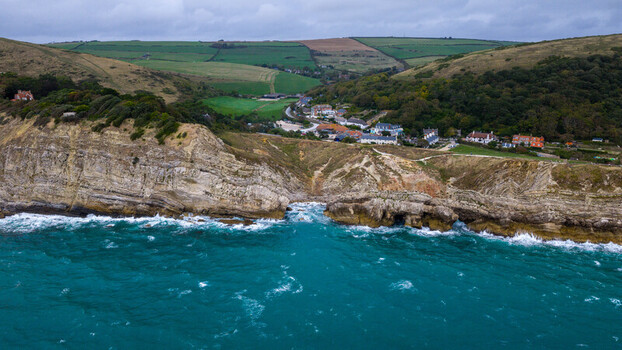 Aerial view of Lulworth Cove featuring turquoise waters dramatic limestone cliffs and lush green hills surrounding the coastal village in the United Kingdom.