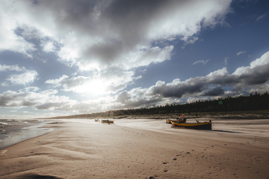 View of fishing boats resting on a sandy beach under a dramatic cloudy sky near a forest line in Debki Pomeranian Voivodeship Poland. View of fishing boats resting on a sandy beach under a dramatic cloudy sky near a forest line in Debki Pomeranian Voivodeship Poland.