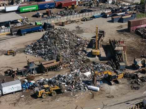 Aerial view of a scrap metal recycling yard with large piles of metal heavy machinery excavators and trucks in an industrial facility in Carson California United States.