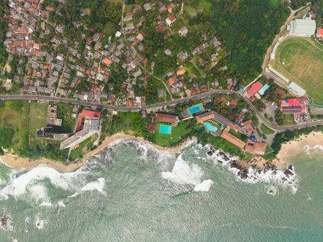 Aerial view of the Galle International Stadium and coastal road winding past residential buildings and lush tropical greenery in Galle Southern Province Sri Lanka. Aerial view of the Galle International Stadium and coastal road winding past residential buildings and lush tropical greenery in Galle Southern Province Sri Lanka.