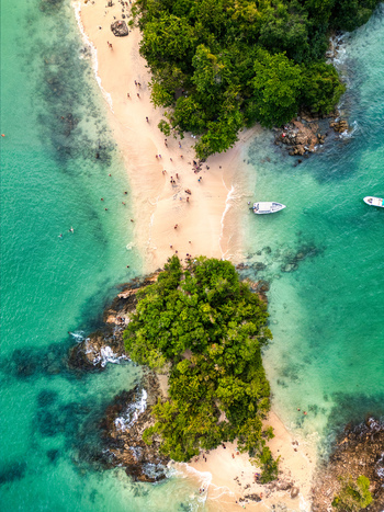 Aerial view of Ilha Cataguas featuring a narrow sandy beach connecting lush green islands surrounded by turquoise tropical waters and small boats Rio de Janeiro Brazil. Aerial view of Ilha Cataguas featuring a narrow sandy beach connecting lush green islands surrounded by turquoise tropical waters and small boats Rio de Janeiro Brazil.