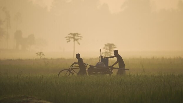 View of people pushing a cart through misty fields Bangladesh.