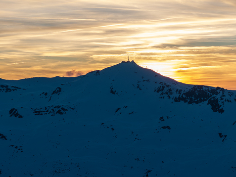 Aerial view of a snow covered mountain silhouette against a fiery sunset sky its peak crowned with structures Val Thorens Auvergne Rh&ocirc;ne Alpes France.