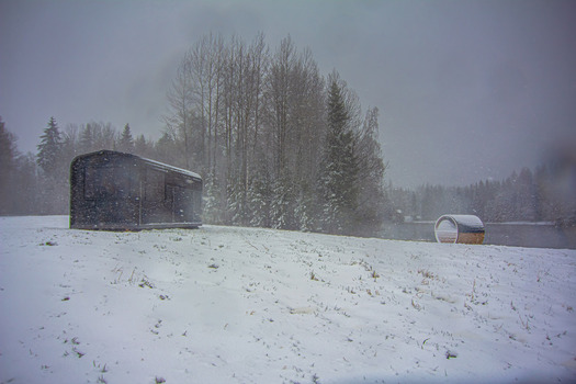 View of a modern cabin and a barrel sauna in a snowy landscape by a lake surrounded by forest in Latvia. View of a modern cabin and a barrel sauna in a snowy landscape by a lake surrounded by forest in Latvia.