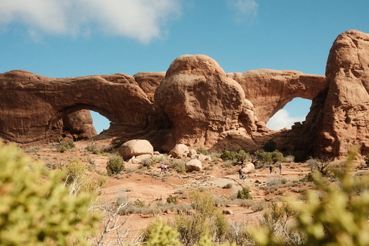 View of the North and South Windows at Arches National Park with tourists walking along desert trails under a blue sky in Grand County Utah United States. View of the North and South Windows at Arches National Park with tourists walking along desert trails under a blue sky in Grand County Utah United States.