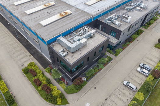 Aerial view of a modern logistics hub with industrial warehouse buildings rooftop ventilation paved parking with cars and landscaped greenery in Skawina Lesser Poland Voivode Poland. Aerial view of a modern logistics hub with industrial warehouse buildings rooftop ventilation paved parking with cars and landscaped greenery in Skawina Lesser Poland Voivode Poland.