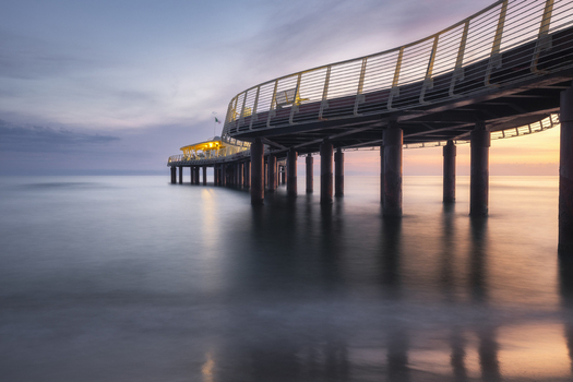View of the modern Pontile di Lido di Camaiore pier stretching over the calm sea at sunset with illuminated railings Lido di Camaiore Tuscany Italy.