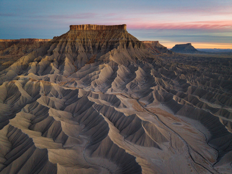 Aerial view of the rugged Caineville badlands featuring dramatic eroded ridges and Factory Butte under a soft sunrise sky in Caineville Utah United States. Aerial view of the rugged Caineville badlands featuring dramatic eroded ridges and Factory Butte under a soft sunrise sky in Caineville Utah United States.