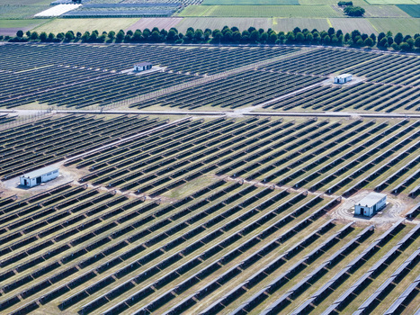 Aerial view of a large solar farm with rows of photovoltaic panels and small utility buildings under bright daylight in Torrazza Piemonte Piemonte Italy. Aerial view of a large solar farm with rows of photovoltaic panels and small utility buildings under bright daylight in Torrazza Piemonte Piemonte Italy.