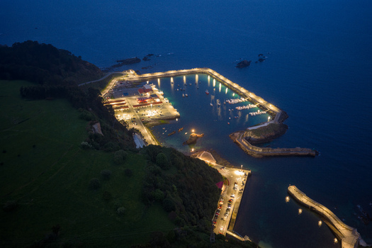 Aerial view of the illuminated harbor of Cudillero at night with boats moored in the calm water and lights reflecting along the stone pier Cudillero Asturias Spain. Aerial view of the illuminated harbor of Cudillero at night with boats moored in the calm water and lights reflecting along the stone pier Cudillero Asturias Spain.