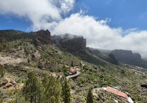 Aerial view of Roque Nublo rising majestically amidst lush green slopes and winding roads under a bright cloud strewn sky La Culata Canarias Spain. Aerial view of Roque Nublo rising majestically amidst lush green slopes and winding roads under a bright cloud strewn sky La Culata Canarias Spain.