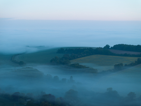 Aerial view of rolling green hills and lush fields shrouded in thick morning mist under a soft dawn sky in Nuffield Oxfordshire United Kingdom. Aerial view of rolling green hills and lush fields shrouded in thick morning mist under a soft dawn sky in Nuffield Oxfordshire United Kingdom.