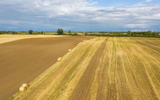 Aerial view of agricultural fields with hay bales plowed soil and harvested stubble under a cloudy sky in Pomeranian Voivodeship Poland.