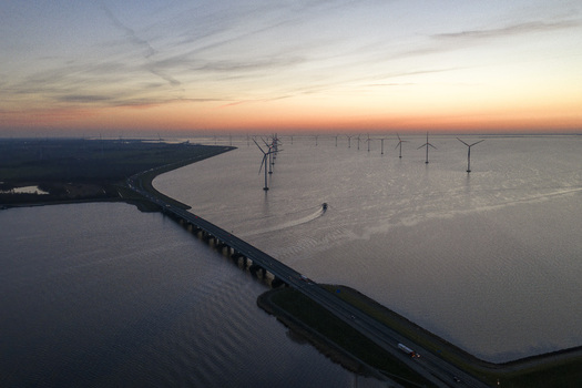 Aerial view of Ketelbrug bridge crossing the Ketelmeer with offshore wind turbines and a boat under a sunset sky Nagele Flevoland Netherlands.