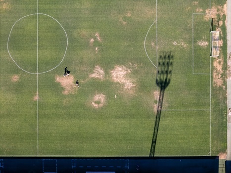 Aerial view of a football field with people walking on the grass and a long shadow cast by a stadium floodlight Elvas Portalegre Portugal. Aerial view of a football field with people walking on the grass and a long shadow cast by a stadium floodlight Elvas Portalegre Portugal.