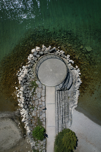 Aerial view of a circular stone viewpoint on the shore of Lake Geneva with clear turquoise water and rocky embankment in Morges Vaud Switzerland. Aerial view of a circular stone viewpoint on the shore of Lake Geneva with clear turquoise water and rocky embankment in Morges Vaud Switzerland.
