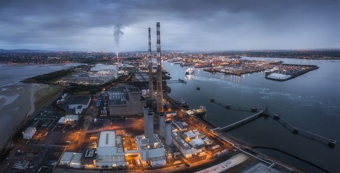 Aerial view of Poolbeg Power Station with its iconic red and white chimneys illuminated at dusk overlooking Dublin Port and the city skyline in Dublin 4 County Dublin Ireland. Aerial view of Poolbeg Power Station with its iconic red and white chimneys illuminated at dusk overlooking Dublin Port and the city skyline in Dublin 4 County Dublin Ireland.