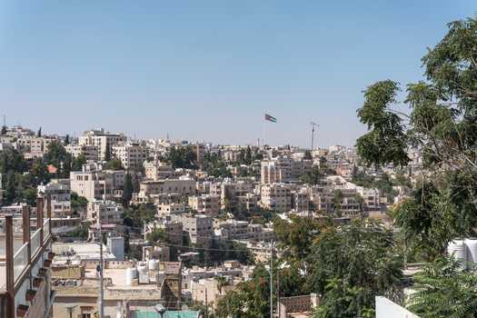 View of the sprawling cityscape of Amman with its characteristic stone buildings lush green trees and the Jordanian flag waving in the distance in Amman Amman Governorate Jordan.