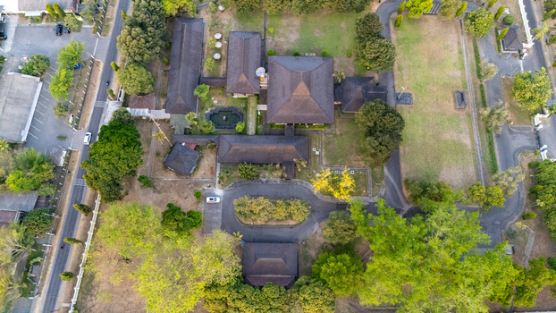 Aerial view of a large building complex with dark tiled roofs surrounded by lush green trees lawns and paved driveways in Indonesia. Aerial view of a large building complex with dark tiled roofs surrounded by lush green trees lawns and paved driveways in Indonesia.