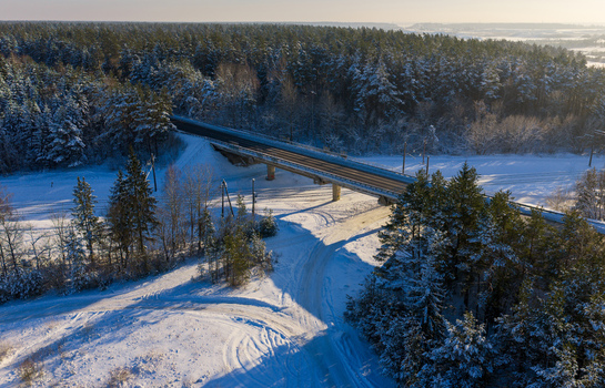 Aerial view of a bridge crossing through a dense snow covered pine forest during a bright winter day in Lithuania. Aerial view of a bridge crossing through a dense snow covered pine forest during a bright winter day in Lithuania.