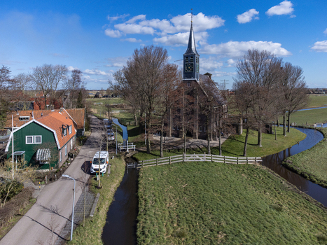 Aerial view of the spire of Hervormde Kerk church piercing the blue sky amidst bare trees juxtaposed against the quaint houses Krommenie Noord Holland Netherlands. Aerial view of the spire of Hervormde Kerk church piercing the blue sky amidst bare trees juxtaposed against the quaint houses Krommenie Noord Holland Netherlands.