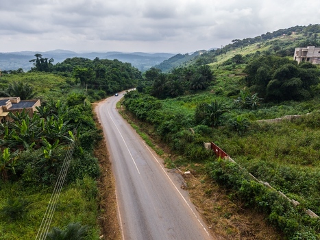 Aerial view of a winding asphalt road cutting through lush tropical vegetation and rolling hills under an overcast sky in Ghana. Aerial view of a winding asphalt road cutting through lush tropical vegetation and rolling hills under an overcast sky in Ghana.