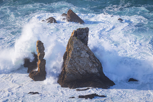View of the jagged rock formations at Silence Beach with crashing white waves and turquoise ocean water in Asturias Spain.