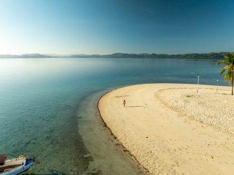 Aerial view of Pass Island with a lone person walking on the white sand beach turquoise water palm tree and distant hills in Coron Philippines. Aerial view of Pass Island with a lone person walking on the white sand beach turquoise water palm tree and distant hills in Coron Philippines.