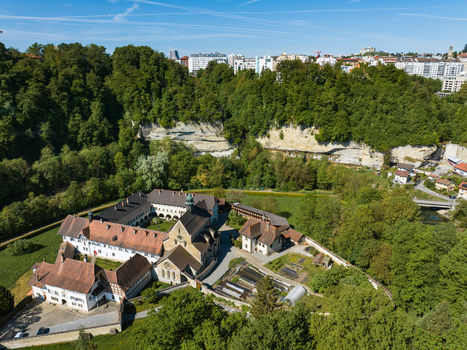 Aerial view of the historic La Maigrauge abbey complex nestled among lush green forests and limestone cliffs under a clear blue sky in Fribourg Fribourg Switzerland. Aerial view of the historic La Maigrauge abbey complex nestled among lush green forests and limestone cliffs under a clear blue sky in Fribourg Fribourg Switzerland.