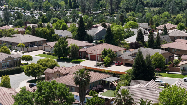 Aerial view of a suburban residential neighborhood featuring single family homes with tiled roofs lush green trees and quiet streets in Redding California United States. Aerial view of a suburban residential neighborhood featuring single family homes with tiled roofs lush green trees and quiet streets in Redding California United States.