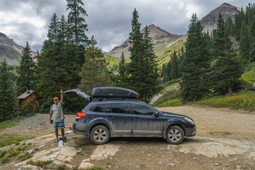 View of a man standing next to a dark SUV with a roof box parked on a rocky trail in the San Juan Mountains near Mount Sneffels Ouray County Colorado United States. View of a man standing next to a dark SUV with a roof box parked on a rocky trail in the San Juan Mountains near Mount Sneffels Ouray County Colorado United States.